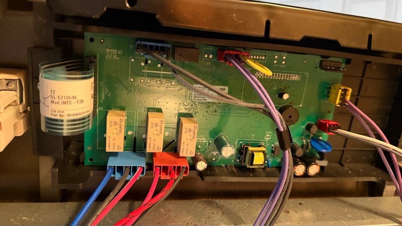 Green electronic control board with various colored wires and beige relays inside a plastic housing.