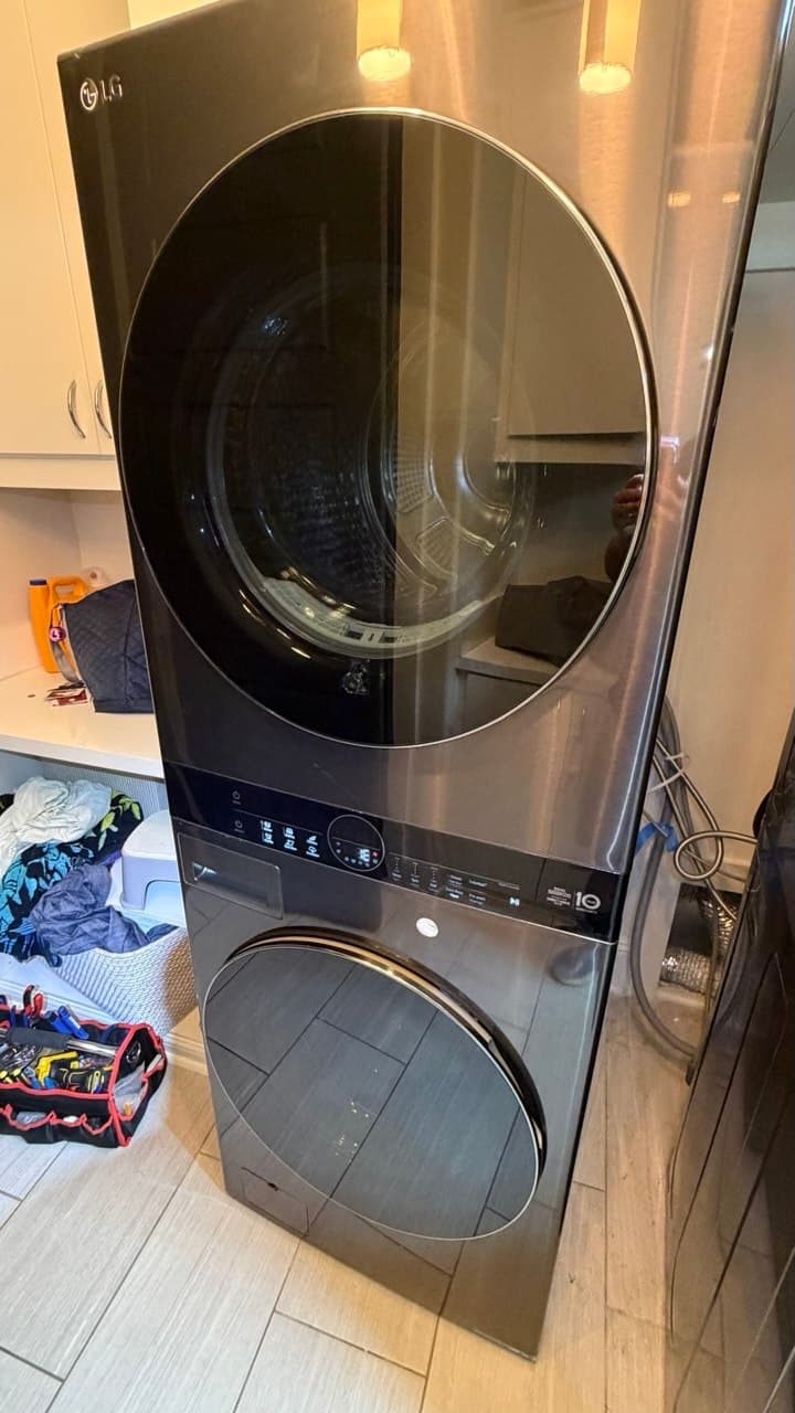Modern dark stainless steel stacked LG washer and dryer unit in a laundry room setting.