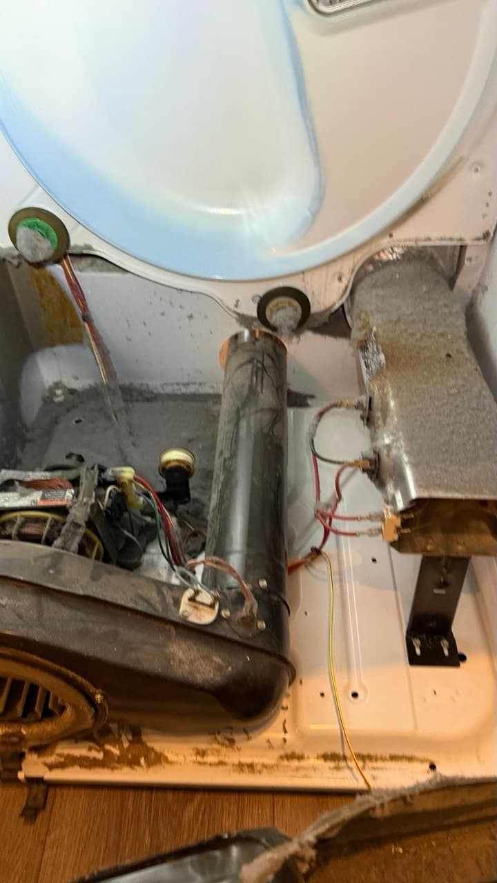 Dusty interior of a disassembled clothes dryer showing the motor, wiring, and lint-covered heating element.