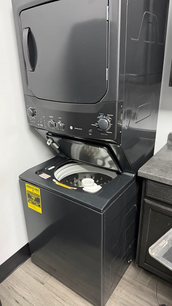 Dark gray stacked washer and dryer unit with the top-loading washing machine lid open.