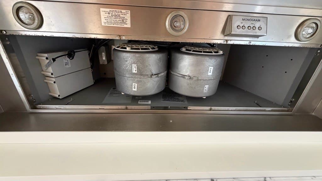 Interior of a Monogram range hood showing dual blower motors and electrical control boxes.