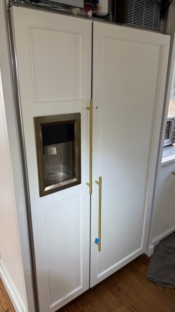 Built-in white refrigerator with shaker panels, sleek gold handles, and an integrated water dispenser.