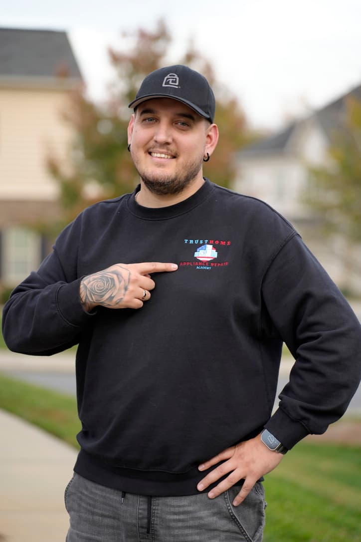 Smiling man in a black sweatshirt points to the TrustHome Appliance Repair Academy logo.