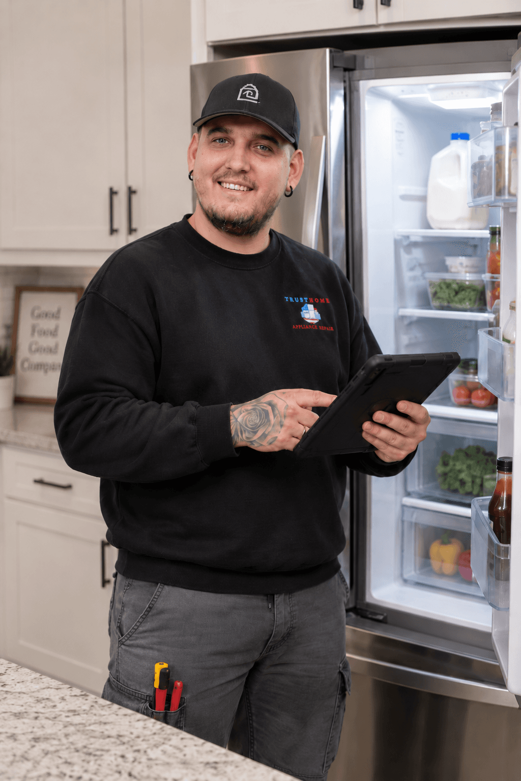 Smiling appliance repair technician holding a tablet in front of an open refrigerator.